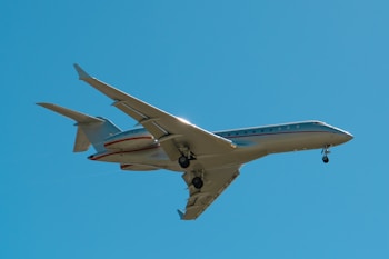 A private jet with extended landing gear flies against a clear blue sky, capturing the sleek design and modern engineering of the aircraft.