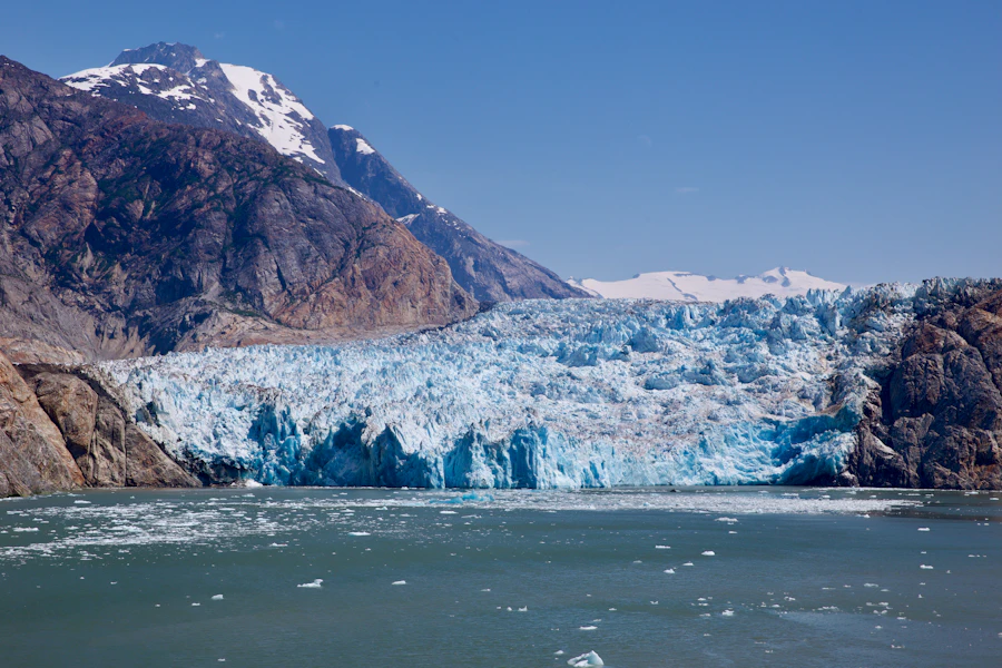 Blue ice glacier spilling between brown mountains into an Alaskan fjord