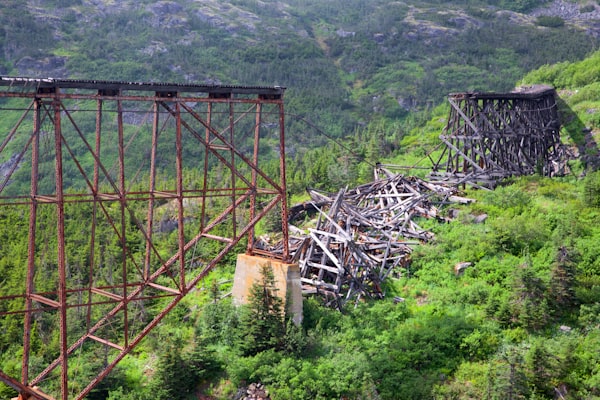 a collapsed section of an elevated railroad track in remote hilly and forested terrain