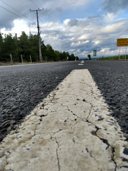 A cracked, worn-out road with deep tire marks from heavy electric vehicles under a cloudy sky.