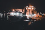 Nighttime shot of a ship illuminated by bright lights while docked for loading.
