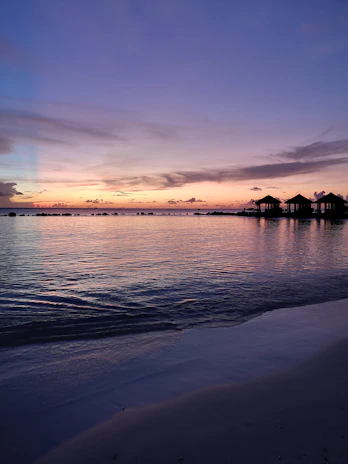 A serene sunset over the turquoise waters of the Maldives, with overwater bungalows glowing softly.
