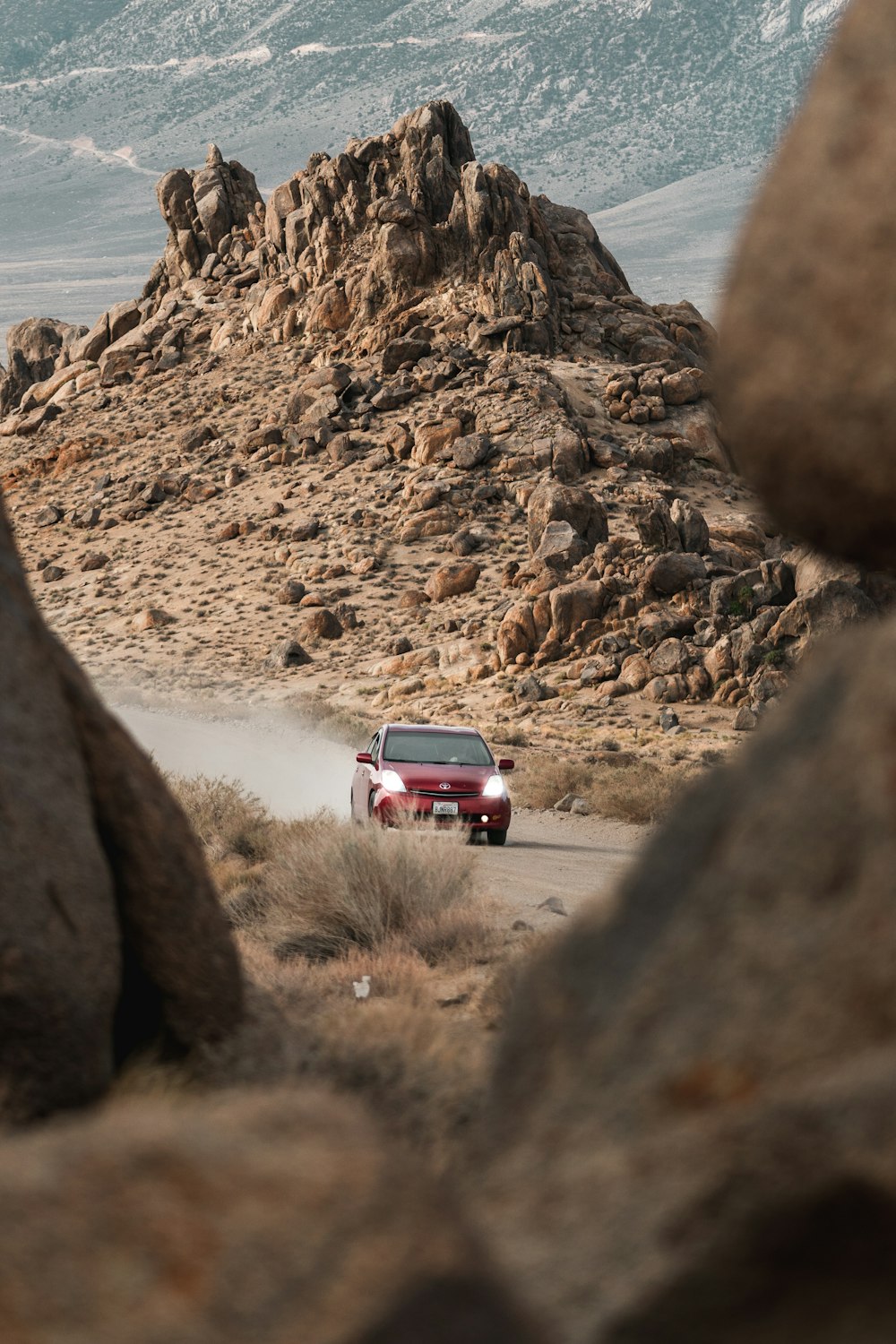 a red car driving on a dirt road between large rocks