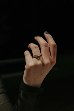 Close-up of a delicate hand adorned with glowing golden rings against a deep midnight blue background.