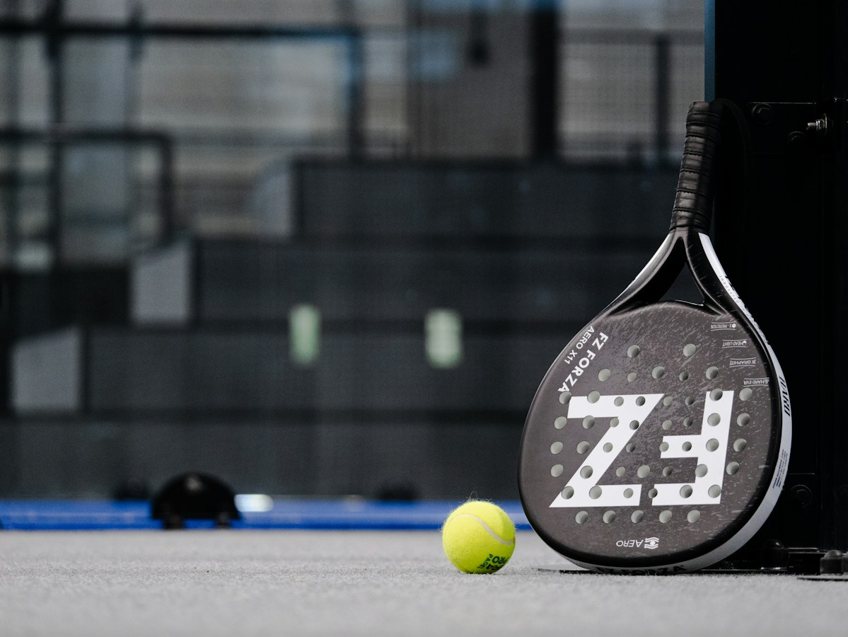 Una paleta de pádel y una pelota amarilla sobre una cancha