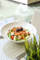 A colorful salad bowl filled with mixed greens, cherry tomatoes, avocado slices, and grilled chicken on a rustic wooden table.