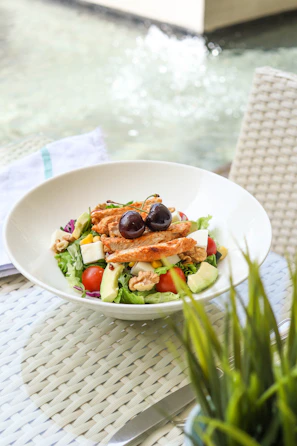 A colorful salad bowl filled with mixed greens, cherry tomatoes, avocado slices, and grilled chicken on a rustic wooden table.