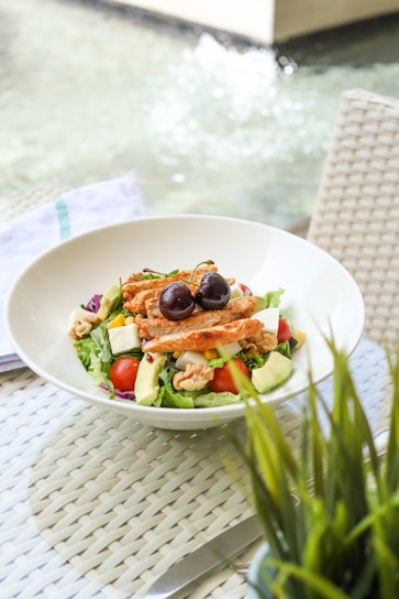 A vibrant bowl of colorful, fresh salad with grilled chicken and avocado slices on a wooden table