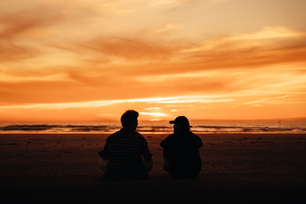 a couple of people sitting on a beach at sunset