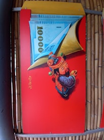 A vibrant red panel features an artistic depiction of a traditional Asian figure in colorful attire, holding a large piece of currency with the number 1000 prominently displayed. The figure is adorned with intricate designs and patterns, symbolizing prosperity or fortune. Chinese characters are written vertically on the panel.