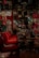 A dimly lit, elegant restaurant interior with red chairs lined up at wooden tables. Wine glasses are neatly arranged, and decorative light fixtures hang from the ceiling. The reflection patterns on glossy surfaces create an upscale ambiance.