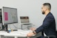 a man sitting at a desk with a laptop and a computer