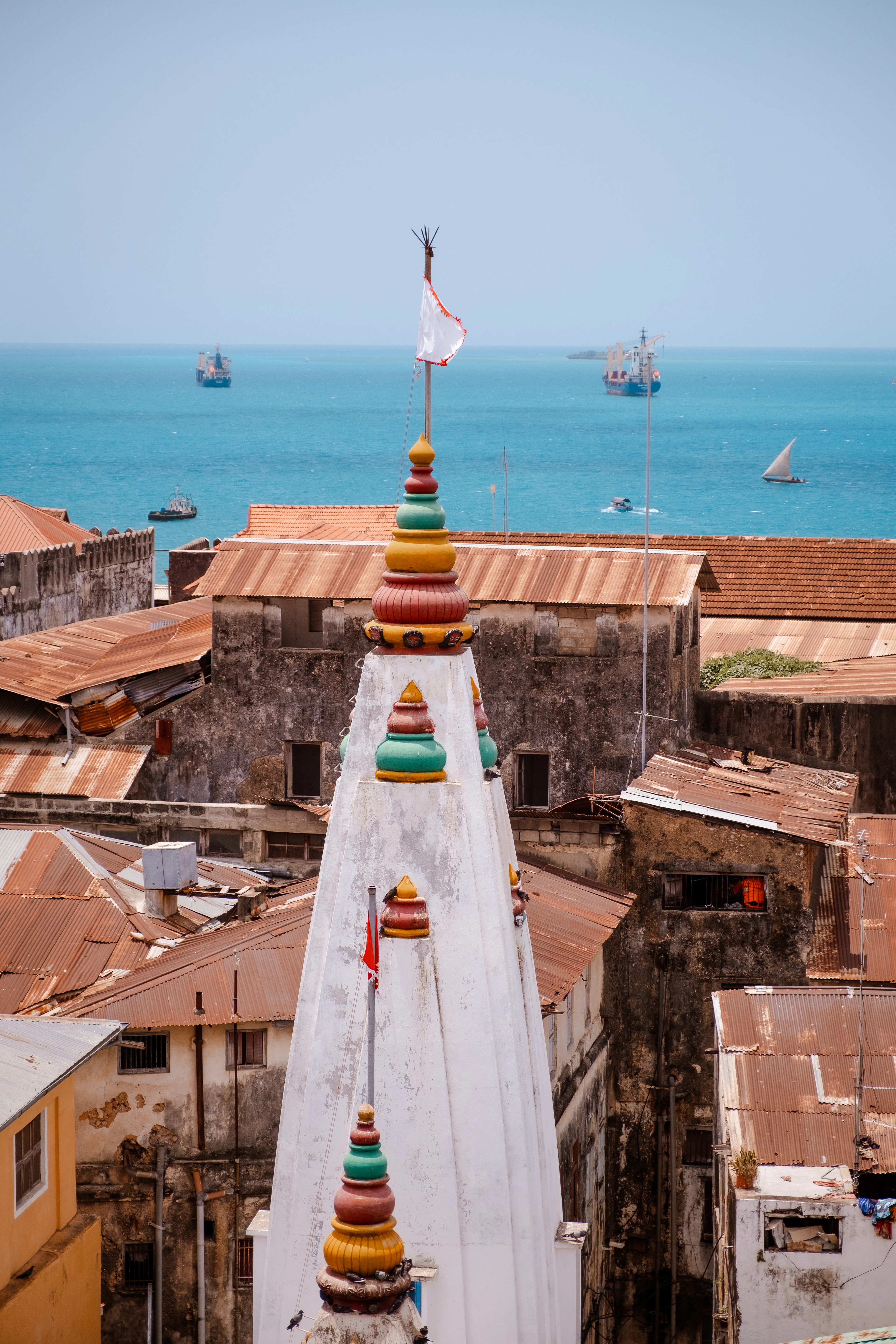 The rusted rooftops of Stone Town, Zanzibar, a temple spire above them and the sea beyond