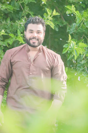 Founder of Vedavooti Organic smiling warmly in a sunlit garden surrounded by medicinal plants.