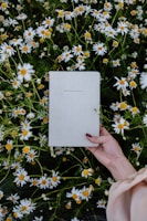 Close-up of hands holding a journal with a pen, surrounded by soft pink flowers.