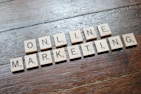 Scrabble tiles arranged to spell 'ONLINE MARKETING' on a wooden table with a textured surface.