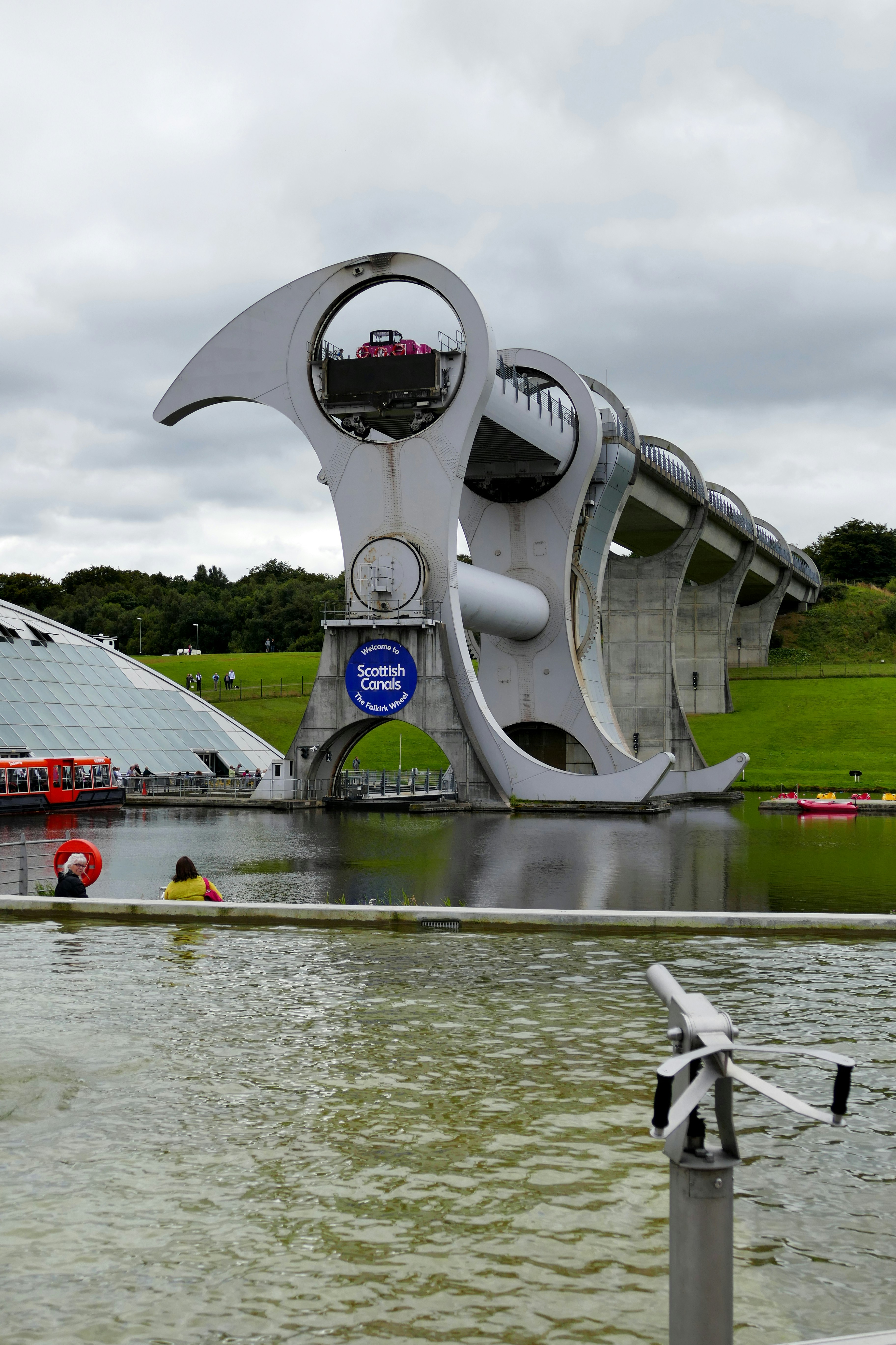 a large white satellite dish in a pond with Falkirk Wheel in the background