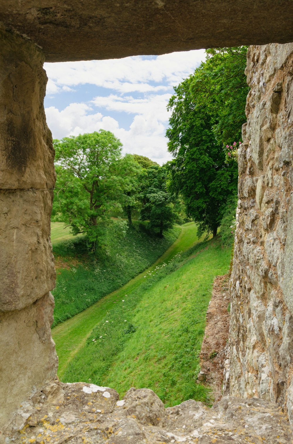 uma vista de um campo verde através de uma parede de pedra