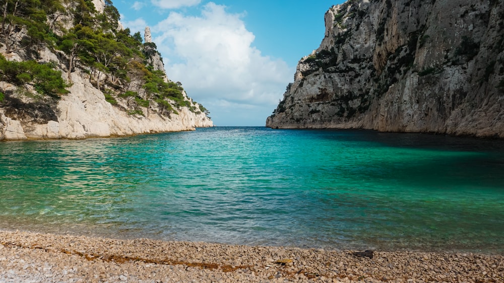 a beach with a rocky cliff and blue water