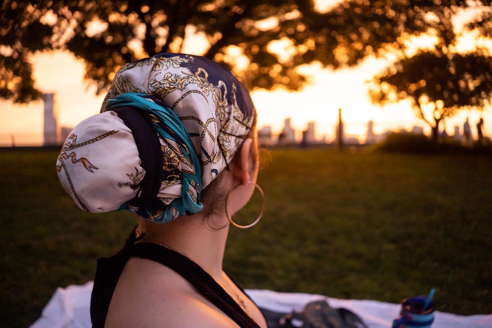 a woman sitting on a blanket in the grass with a sunset in the background