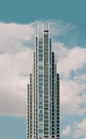 A modern, tall skyscraper with a series of tiered sections rising against a backdrop of a blue sky with scattered white clouds.