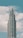 A modern, tall skyscraper with a series of tiered sections rising against a backdrop of a blue sky with scattered white clouds.