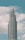 A modern, tall skyscraper with a series of tiered sections rising against a backdrop of a blue sky with scattered white clouds.