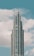 A modern, tall skyscraper with a series of tiered sections rising against a backdrop of a blue sky with scattered white clouds.