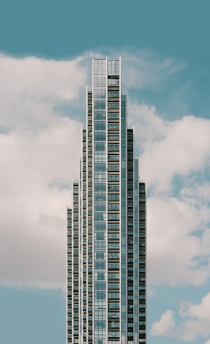 A modern, tall skyscraper with a series of tiered sections rising against a backdrop of a blue sky with scattered white clouds.