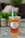 A plastic cup filled with iced tea or boba tea labeled 'Happy Boba' with a green straw. The drink has a lemon slice and appears to have boba or jelly pieces at the bottom. It is placed on a marble or granite surface with a blurred background featuring greenery and soft furnishings.