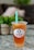 A plastic cup filled with iced tea or boba tea labeled 'Happy Boba' with a green straw. The drink has a lemon slice and appears to have boba or jelly pieces at the bottom. It is placed on a marble or granite surface with a blurred background featuring greenery and soft furnishings.