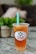 A plastic cup filled with iced tea or boba tea labeled 'Happy Boba' with a green straw. The drink has a lemon slice and appears to have boba or jelly pieces at the bottom. It is placed on a marble or granite surface with a blurred background featuring greenery and soft furnishings.
