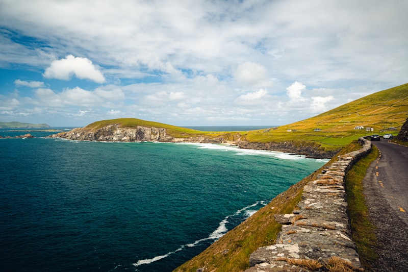 The Slea Head road curving above cliffs with a sandy cove and green headlands beyond