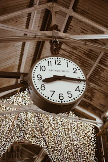 A farmhouse-style metal wall clock hanging above a rustic dining table with warm lighting.