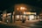 A corner building with a mini mart named Marie's is illuminated by street lamps at night. The structure includes a business sign and other advertisements. It is surrounded by deserted streets and a few parked cars. The building has a brick facade with multiple windows.