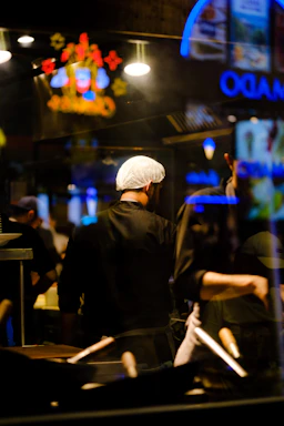 Close-up of a chef’s hand adjusting a compact LED light over a sizzling pan in a busy kitchen.