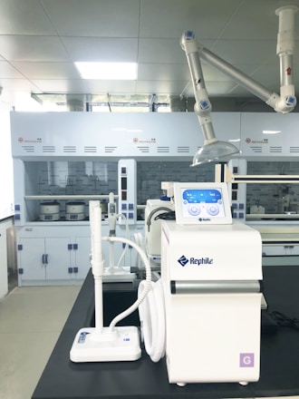A laboratory setting featuring advanced equipment, including a white Rephile machine with digital controls and various attachments. In the background, there are large lab cabinets and ventilation hoods, with a bright, well-lit environment.
