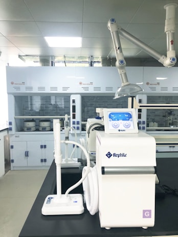 A laboratory setting featuring advanced equipment, including a white Rephile machine with digital controls and various attachments. In the background, there are large lab cabinets and ventilation hoods, with a bright, well-lit environment.