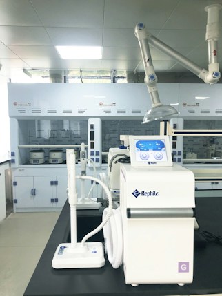 A laboratory setting featuring advanced equipment, including a white Rephile machine with digital controls and various attachments. In the background, there are large lab cabinets and ventilation hoods, with a bright, well-lit environment.