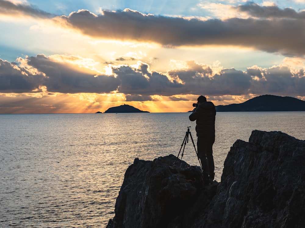 a man standing on a rock looking at the sunset