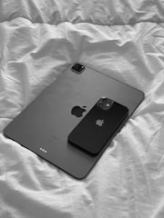 A black tablet and smartphone are placed side by side on a white, wrinkled bed sheet, showcasing a minimalist design.