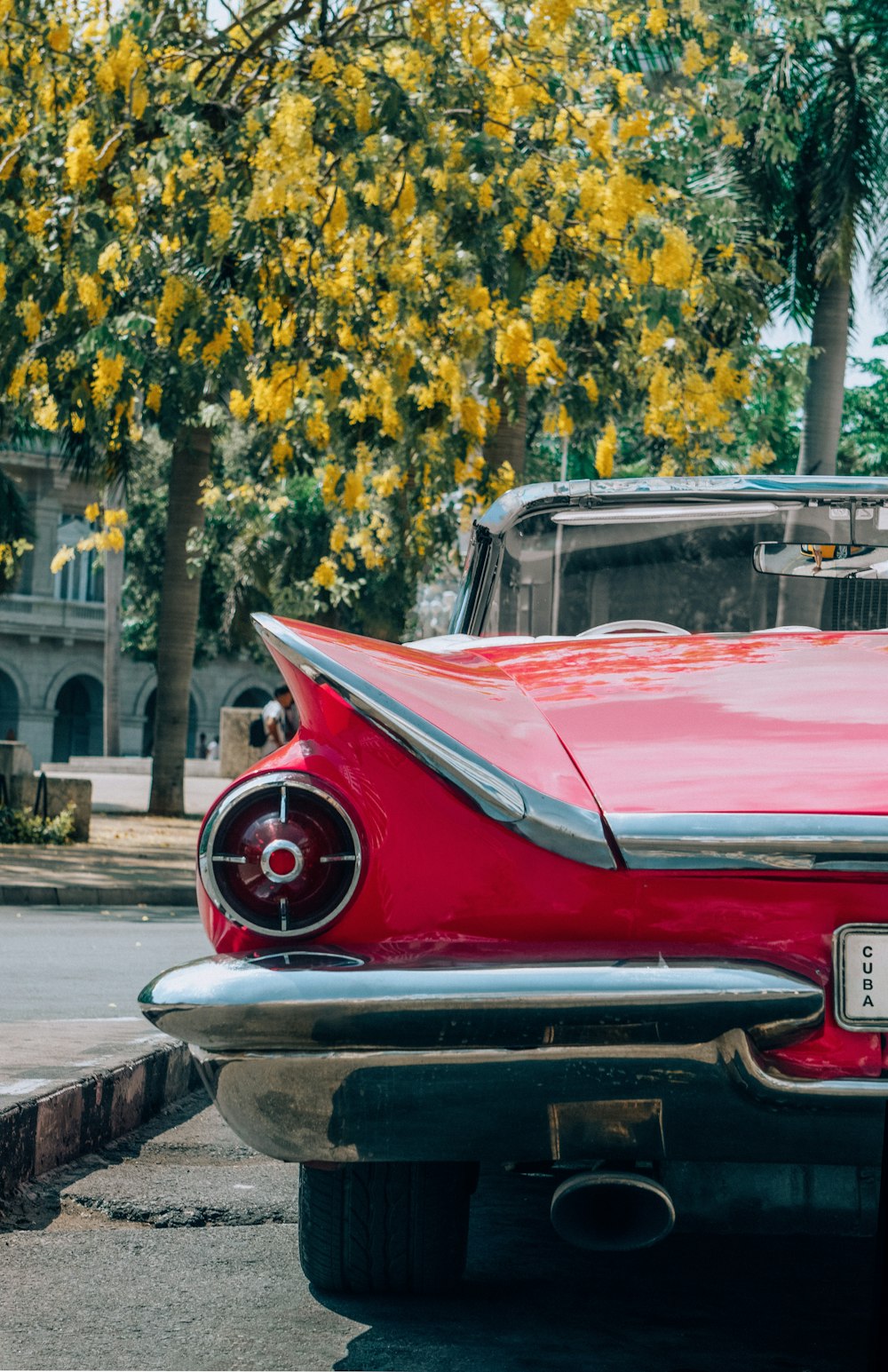 a red car parked in front of a tree with yellow leaves