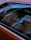 The interior of a car is visible through the window, showcasing a steering wheel, dashboard, and leather seats. The seats and interior elements appear in neutral tones, and there's a reflection of outdoor trees on the window.