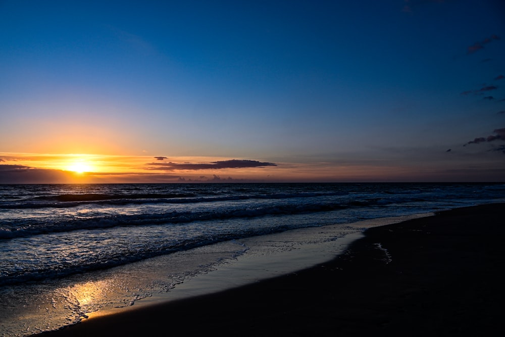 a beach with waves and the sun setting