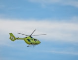 A bright yellow helicopter is flying against a clear blue sky. The helicopter has emergency medical service markings and is seen with its rotors in motion.