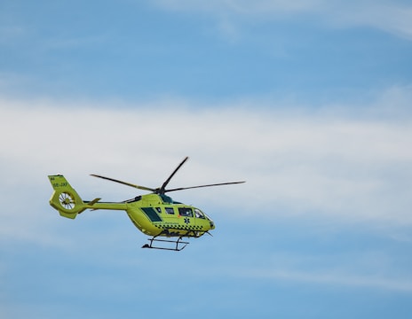 A bright yellow helicopter is flying against a clear blue sky. The helicopter has emergency medical service markings and is seen with its rotors in motion.