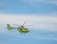 A bright yellow helicopter is flying against a clear blue sky. The helicopter has emergency medical service markings and is seen with its rotors in motion.