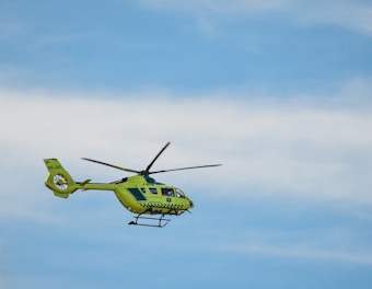 A bright yellow helicopter is flying against a clear blue sky. The helicopter has emergency medical service markings and is seen with its rotors in motion.