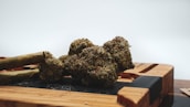A close-up of a cannabis bud with two rolled blunts next to it, placed on a wooden surface.