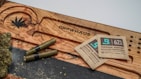 A wooden surface with a carved cannabis leaf and the word 'Growhaus'. There are several cannabis joints and buds next to two terpene shield humidity packets.